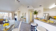This well-appointed single-floor residence offers an inviting open-concept layout that seamlessly connects the living, dining, and kitchen areas. The living room immediately stands out with its soaring vaulted ceilings and track lighting, creating a bright, airy atmosphere enhanced by plush carpeting and generous natural light filtering through large windows with sheer curtains. A fireplace serves as a classic focal point, adding warmth and character to the living space.

The kitchen is efficiently designed with white cabinetry, stainless steel appliances including a refrigerator, microwave, and range, and dark granite countertops. A raised breakfast bar with stylish barstool seating provides a casual dining option and connects the kitchen to the main living area.

Both bedrooms offer comfortable carpeted flooring and natural light. The primary bedroom features a window with outdoor views, while the second bedroom benefits from vaulted ceilings, adding a sense of spaciousness. The bathroom is well-equipped with a soaking tub, a separate shower, tile flooring, and a framed wall mirror, offering a functional and relaxing retreat.

Throughout the residence, a neutral color palette of warm whites and beige tones creates a cohesive and welcoming ambiance, making this a practical and comfortable living space.