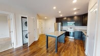 Located at 3730 Evergreen Dr in Monroeville, PA, this well-appointed single-floor residence offers a thoughtfully designed layout with modern finishes throughout. The kitchen serves as a central highlight, featuring dark shaker-style cabinetry, granite countertops, a central island with bar seating, and a full suite of stainless steel appliances including a refrigerator, electric range, built-in microwave, and dishwasher. Recessed lighting illuminates the space, which flows seamlessly onto rich hardwood flooring extending through the main living areas. A dedicated in-unit laundry closet with a stacked washer and dryer adds everyday convenience. The open living area is bathed in natural light from large windows and a glass door that offers outdoor views of lush greenery, creating a bright and airy atmosphere. The bedroom is carpeted for comfort and features a generous walk-in closet with built-in wire shelving. Two bathrooms echo the home's consistent design aesthetic, each finished with classic black-and-white penny tile flooring and dark vanity cabinetry. The primary bathroom includes a dual-sink vanity with a large mirror, while the second bath provides a single-sink vanity. Clean white walls and crisp trim throughout lend the space a fresh, contemporary feel.