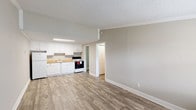 This single-floor unit offers a clean, functional layout designed for comfortable everyday living. The open-concept living and dining area flows directly into the kitchen, creating a connected, airy feel. Wood-look vinyl plank flooring runs consistently throughout the space, complemented by neutral warm-gray walls, crisp white baseboards, and crown molding that add a polished finish.

The kitchen is well-appointed with white cabinetry offering ample storage, warm-toned countertops, a built-in sink, and a full suite of appliances including a refrigerator and electric range. A flush-mounted ceiling light provides bright, even illumination over the workspace.

The living area features a front entry door flanked by a window fitted with blinds, allowing natural light to filter in. A wall-unit HVAC system ensures year-round climate control. The bedroom is a comfortable, well-proportioned room with its own window and a ceiling fan with integrated lighting for added comfort.

The bathroom includes a vanity with storage, a toilet, and a shower-tub combination. A separate utility room houses the water heater, keeping mechanical elements neatly contained. The textured popcorn ceilings and crown molding are consistent throughout, tying the entire space together with a cohesive design aesthetic.