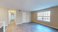 This single-floor unit offers a thoughtfully designed layout that balances open communal spaces with private living areas. The living room is a bright, welcoming space featuring smooth light gray hardwood-style flooring, neutral beige walls, and a generously sized window that draws in natural light and provides views of the surrounding exterior. A closet door off the main living area adds practical storage within easy reach.

The kitchen is a standout feature, showcasing rich dark espresso cabinetry that extends from floor to ceiling, contrasted by light countertops and a functional peninsula with a built-in sink — ideal for casual dining or meal preparation. Stainless steel appliances, including a refrigerator, electric range, and dishwasher, complete the space with a modern, cohesive aesthetic. Light wood-style flooring ties the kitchen seamlessly into the adjoining living area.

The bedrooms continue the home's clean, neutral palette, featuring plush gray carpet for added comfort and windows that invite natural light. Each room offers a calm, versatile environment suitable for rest or work.

The bathroom is finished with light wood-style flooring, a warm wood-toned vanity with white countertop, a wall mirror, and a full tub-shower combination with chrome fixtures. The space is clean and functional throughout.