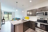 Located at 409 S 48th St in Lincoln, Nebraska, this well-designed one-bedroom, one-bathroom unit offers a thoughtfully arranged single-floor layout that makes excellent use of its compact footprint. Light-toned wood-style flooring flows throughout the main living areas, lending a clean, contemporary feel to the space.

The kitchen is a standout feature, equipped with stainless steel appliances — including a full-size refrigerator, electric range, and built-in microwave — dark espresso cabinetry, white quartz countertops, and a peninsula with bar seating, ideal for casual dining. Recessed lighting and a pendant fixture brighten the workspace efficiently.

The living room benefits from large floor-to-ceiling windows that invite abundant natural light and offer pleasant views of the surrounding tree canopy, creating a bright and airy atmosphere. The bedroom mirrors this quality, featuring its own oversized window with exterior views and plush carpeting for added comfort.

The bathroom is finished with wood-look tile flooring, dark cabinetry with a vanity, matte black hardware accents, and a walk-in shower. A dedicated in-unit laundry area houses a full-size side-by-side washer and dryer, adding everyday convenience. The overall design is modern, clean, and functionally efficient.