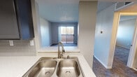 This single-floor residential unit offers a functional and well-appointed layout designed for comfortable everyday living. The kitchen is a standout feature, outfitted with dark charcoal cabinetry, light-toned quartz-style countertops, a classic subway tile backsplash, stainless steel appliances including a full-size refrigerator and dishwasher, and wood-look flooring. A double-basin stainless steel sink with a gooseneck faucet is positioned at a pass-through opening, creating a natural visual connection to the living area. The living room is spacious and carpeted, with neutral walls, a textured ceiling, and a sliding glass door that opens to a private balcony, allowing for an abundance of natural light and outdoor views. A pass-through window from the kitchen adds an open, connected feel between the two spaces. The bedroom is generously sized, featuring plush carpet, neutral gray walls, a textured ceiling, and a window that brings in additional natural light. The bathroom is clean and efficiently designed, with wood-look flooring, a full soaking tub with a shower and curtain rod, a white vanity with a light countertop, a large mirror, and warm neutral wall tones. Overall, the unit presents a cohesive, move-in-ready aesthetic with updated finishes throughout.