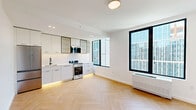 Located at 104 Fleet Pl in the heart of Downtown Brooklyn, this thoughtfully designed one-bedroom, one-bathroom residence offers a clean, modern aesthetic throughout. The open-plan living and kitchen area is anchored by striking herringbone-patterned hardwood floors and crisp white walls, creating a bright and airy atmosphere. Large black-framed windows invite generous natural light and frame views of the surrounding Brooklyn skyline.

The contemporary kitchen is a standout feature, outfitted with sleek white flat-front cabinetry accented by black hardware, open upper shelving, a white quartz countertop, and stainless steel appliances including a range and French door refrigerator. Subtle under-cabinet LED lighting adds a warm, refined touch.

The bedroom is a calm, well-proportioned retreat bathed in natural light from floor-to-ceiling windows overlooking the urban cityscape. A hallway connects the living spaces efficiently, maintaining a smooth flow throughout the residence.

The bathroom is a design highlight, featuring floor-to-ceiling vertical tile, a soaking tub with an integrated shower, a warm wood-toned floating vanity on a black metal frame, terrazzo-style flooring, and globe pendant lighting — all combining to create a spa-like ambiance. Every detail of this residence reflects a commitment to modern urban living.
