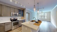 Located at 2875 Crescent Pkwy in Atlanta, Georgia, this well-appointed two-bedroom, two-bathroom residence offers a thoughtfully designed single-floor layout with a seamless flow between living spaces. The open-concept kitchen is a standout feature, showcasing gray shaker-style cabinetry, stainless steel appliances, a classic white subway tile backsplash, and a large center island with quartz countertops and a gold-toned faucet. Elegant pendant lighting hangs above the island, complementing the track lighting overhead. Warm hardwood-style flooring extends through the kitchen and living areas, while the living room benefits from multiple windows and a glass-panel door that invite abundant natural light and views of surrounding greenery. Crown molding and a ceiling fan add refined detail to the living space. The bedrooms are carpeted for comfort, with windows framing peaceful outdoor views. The primary bedroom is generously proportioned and connects to a bathroom featuring a soaking tub with subway tile surround, tile flooring, and direct access to a walk-in closet with wire shelving. The second bathroom mirrors this clean, classic aesthetic. Hallways connect all areas efficiently, completing a practical and polished floor plan.