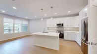 This thoughtfully designed single-floor residence offers a clean, modern aesthetic throughout its well-appointed layout. The open-concept kitchen serves as the heart of the home, showcasing crisp white shaker cabinetry, a neutral tile backsplash, stainless steel appliances — including a gas range, microwave, and refrigerator — and a generous center island with a built-in sink and pendant lighting overhead. Light wood-tone flooring flows seamlessly through the kitchen and into the living area, which benefits from natural light through large windows and access to an outdoor balcony. A ceiling fan enhances comfort in the bedroom, which is a well-proportioned retreat featuring the same warm hardwood-style flooring and a dedicated walk-in closet outfitted with built-in shelving, hanging rods, and ample storage space. Both bathrooms are finished with striking marble-look tile flooring, floating white vanities with dual sinks, large framed mirrors, and glass-enclosed showers, lending a spa-like quality to the space. Recessed lighting throughout and a neutral color palette of whites and soft grays create a bright, cohesive ambiance that feels both modern and welcoming.