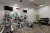 Located at Telephone Factory Lofts — a historic property established in 1938 — on Ralph McGill Boulevard in Atlanta, GA, this well-equipped fitness center offers residents a convenient and functional space to maintain an active lifestyle. The room is finished with a drop tile ceiling, recessed lighting, and ceiling fans that help maintain a comfortable environment during workouts. A wall-mounted split AC unit provides additional climate control.

The fitness center is outfitted with a variety of cardio equipment, including treadmills, an elliptical trainer, and a stationary bike, each positioned on protective floor mats atop the patterned, multi-tone carpet. A cable machine and weight bench round out the strength training options, while a tiered dumbbell rack and kettlebell set offer a full range of free weight choices. Stability balls and a yoga mat are also available for stretching and functional fitness work.

Full-length mirrors line one wall, amplifying the sense of space and allowing users to monitor their form during exercise. Multiple flat-screen TVs are mounted on the walls, providing entertainment options throughout any workout. A bold, circular rotary dial graphic — a nod to the building's telephone factory heritage — serves as a striking mural on the exposed painted brick accent wall, adding character and a sense of place to the space.