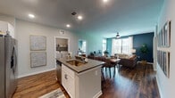 This single-floor residence offers a thoughtfully designed open-concept layout that seamlessly connects the kitchen, dining, and living areas. The kitchen is a standout feature, equipped with crisp white shaker cabinets, granite-style countertops, a mosaic tile backsplash, stainless steel appliances including a range, microwave, and refrigerator, and a central island with a built-in sink. Rich hardwood-style flooring runs throughout the main living areas, complementing the bold teal and navy accent walls that lend the space a vibrant, contemporary character. The living room is bright and welcoming, with large windows that invite generous natural light and provide outdoor views, while a ceiling fan adds functional comfort. A dedicated dining area flows naturally from the kitchen and living room. The bedrooms are carpeted for warmth and comfort, each featuring large windows with outdoor views and ceiling fans. The bathrooms are finished with white cabinetry, dark countertops, and hardwood-style flooring, with one bathroom offering a full tub-shower combination. A dedicated in-unit laundry area adds everyday convenience. Throughout the residence, recessed lighting, clean trim work, and consistent modern finishes create a cohesive and inviting atmosphere.