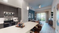Located at 600 N Pine Island Rd in Plantation, FL, this single-floor residence offers a thoughtfully designed open-concept layout with contemporary finishes throughout. The kitchen is a standout feature, equipped with full-height gray shaker cabinetry, stainless steel appliances including a French door refrigerator, electric range, built-in microwave, and dishwasher. A white quartz island with bar seating and pendant lighting serves as both a functional workspace and a casual dining area. Light wood-style flooring flows seamlessly from the kitchen into the living area, which is anchored by a bold teal accent wall, adding depth and character to the space. Sliding glass doors open to a private balcony, allowing natural light to pour in and offering views of lush tropical greenery. The bedroom is a calm retreat, featuring a dark accent wall, plush carpeting, and a large window framing palm tree views. The bathroom is finished with large-format tile flooring, dual-sink gray vanity with white countertops, and direct access to a spacious walk-in closet with built-in shelving and hanging storage. The overall design balances modern aesthetics with functional living in a vibrant South Florida setting.