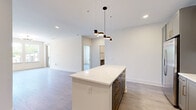 This well-appointed single-floor residence offers three bedrooms and three bathrooms within a thoughtfully designed open-concept layout. The combined kitchen and living area serves as the heart of the home, anchored by a striking central island topped with veined white quartz countertops and accented by a row of modern matte black pendant lights. The kitchen features grey cabinetry with gold-toned hardware, a textured herringbone tile backsplash, stainless steel appliances including a French-door refrigerator, and a matte black faucet — delivering a clean, contemporary aesthetic. Light hardwood-style flooring runs continuously throughout the space, contributing to a bright and cohesive feel. Each of the three bedrooms is finished with the same flooring and neutral walls, with multiple bedrooms benefiting from large windows that frame views of mature trees and greenery, filling the rooms with natural light. The primary bedroom offers a comfortable footprint with a dedicated sputnik-style light fixture. The bathrooms are finished to a high standard, showcasing grey vanity cabinetry with white quartz counters, matte black fixtures and hardware, LED-backlit mirrors, large-format porcelain tile flooring, and a soaking tub with tiled surround. Throughout the home, clean lines, neutral tones, and modern finishes create a consistent and polished living environment.