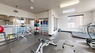 Located at 1758 6th Ave in Greeley, Colorado, this single-floor fitness center offers a well-organized and fully equipped workout space designed to support a wide range of exercise routines. The gym features durable speckled rubber flooring throughout, providing a safe and functional surface for all types of training activities.

The space is thoughtfully divided into distinct workout zones. The cardio area includes treadmills, an elliptical trainer, and a stationary spin bike, positioned near large windows that allow natural light to fill the room and offer views of the surrounding exterior. A dedicated free weights section features a full dumbbell rack alongside adjustable workout benches, while a multi-station cable machine provides options for comprehensive strength training.

A mirrored wall panel enhances the sense of space and supports form monitoring during exercises. Medicine balls and stability balls are neatly stored on a vertical rack, and additional storage cubbies keep the area organized. The gym is brightly lit with overhead fluorescent and recessed lighting, maintaining a clean and energetic atmosphere.

A glassed-in alcove near the entrance houses a beverage vending machine, adding convenience for users. The white walls and modern finishes contribute to a clean, professional aesthetic. This well-maintained facility delivers a complete workout experience within a compact and efficiently utilized footprint.