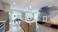 Located at 300 Parkway Dr in Buffalo Grove, IL, this single-floor residence offers a thoughtfully designed open-concept layout with contemporary finishes throughout. The kitchen serves as a central hub of the living space, anchored by a large island with a white quartz countertop, undermount sink, and seating for multiple guests. Track pendant lighting, wood-toned cabinetry, a subway tile backsplash, stainless steel appliances, and a built-in wine refrigerator elevate the kitchen's functionality and style. Light hardwood flooring flows seamlessly into the dining area, where large windows dressed in linen curtains frame views of the surrounding greenery and courtyard. The living room features a sliding glass door opening to a private balcony, flooding the space with natural light. A bold watercolor wall mural adds an artistic focal point to the main living area. The bedrooms offer plush carpeting and large windows with serene tree-lined views. One bedroom is highlighted by a dramatic, full-wall portrait mural. The bathroom features wood-grain cabinetry, white quartz surfaces, light tile flooring, and direct access to a walk-in closet, completing this modern and well-appointed residence.