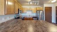 Located at 1250 Mountain Bay Dr in Pulaski, Wisconsin, this single-floor unit offers a functional and comfortable layout with a variety of practical features throughout. The kitchen serves as a central highlight, equipped with stainless steel appliances including a refrigerator, electric range, microwave, and dishwasher. Warm-toned wood cabinetry provides generous storage, while stone-finish countertops extend to a peninsula island, adding prep space and an open connection to the surrounding living area. Track lighting overhead brightens the workspace effectively.

The living area features durable wood-look flooring, a sliding glass door that invites natural light and outdoor views, and a baseboard heating system. Adjacent entry doors provide convenient access points. Bedrooms are finished with plush carpeting and include closets with built-in shelving and hanging rods, along with windows fitted with blinds that frame outdoor views.

Two bathrooms serve the unit: one features wood-look flooring, a walk-in shower, and wood cabinetry, while the second includes a tub-shower combination and a vanity with a stone-finish countertop. A dedicated laundry area houses a full-size Whirlpool washer and dryer with overhead cabinetry for additional storage, completing this well-organized and practical living space.