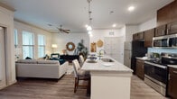 This single-floor residence offers a thoughtfully designed open-concept layout that seamlessly connects the kitchen, dining, and living areas. The kitchen is a functional centerpiece, featuring dark espresso cabinetry, granite countertops, stainless steel appliances, and a large island with an integrated sink and bar seating — ideal for both meal preparation and casual dining. Pendant lighting above the island and recessed ceiling lights provide ample illumination throughout.

The living area flows naturally from the kitchen, offering a bright and welcoming atmosphere enhanced by multiple windows with plantation-style blinds that allow abundant natural light. Crown molding accents the ceiling, and a ceiling fan adds to the comfort of the space. Warm-toned wood-look flooring runs consistently throughout the main living areas.

The bedroom is generously proportioned, providing ample space for a full suite of furniture. A walk-in closet with built-in shelving offers practical storage. The primary bathroom is well-equipped with a dual-sink vanity topped with granite, dark espresso cabinetry, a large mirror, contemporary lighting, and a glass-enclosed walk-in shower. Wood-look flooring continues into the bathroom, maintaining a cohesive aesthetic throughout the residence.