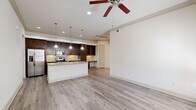 This thoughtfully designed single-story home offers a comfortable and functional layout across its one floor. The open-concept kitchen and living area serves as the heart of the home, featuring rich dark-stained cabinetry, granite countertops, a central island with an undermount sink, and stainless steel appliances. Pendant lighting illuminates the island, while a built-in desk area with open shelving provides a practical workspace. Light-toned hardwood-style flooring flows throughout the main living areas, complemented by crown molding and a ceiling fan that enhance the space's refined character. The bedroom is generously sized, finished with plush carpet, a ceiling fan, and natural light from dual windows. A walk-in closet with wrap-around shelving and hanging rods offers substantial storage. The full bathroom impresses with a dual-sink vanity topped with granite, dark cabinetry, tile flooring, and an arched soaking tub alcove. Hallways connect the spaces efficiently, and an attached single-car garage with an automatic opener provides secure, convenient parking. Neutral tones and consistent finishes throughout create a cohesive, move-in-ready ambiance.