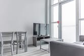 Located at 275 Larch St in Waterloo, Ontario, this efficiently designed one-bedroom, one-bathroom unit offers a thoughtful layout across a single floor. The interior features light-toned laminate flooring throughout, white walls, and soaring ceilings that enhance the sense of openness despite the compact footprint.

The kitchen is well-appointed with dark grey cabinetry, a subway tile backsplash, granite-look countertops, and a full suite of stainless steel appliances including an electric range, dishwasher, and bottom-freezer refrigerator. A track lighting fixture overhead provides focused illumination. The kitchen flows naturally into the living area, which benefits from floor-to-ceiling windows and a glass door that flood the space with natural light and offer access to the outdoors.

The bedroom is a quiet, cozy retreat featuring large gridded windows that bring in diffused natural light. The bathroom includes a full-sized soaker tub and shower combination with built-in shelving and clean white surround panels.

Overall, the unit presents a modern, minimalist aesthetic with a neutral palette, making it a functional and bright living space well-suited to those seeking efficient urban living in the Waterloo region.