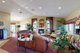Located at 26 Sea Breeze Dr in South Dartmouth, MA, this generously sized single-floor community clubhouse offers a comprehensive range of amenities across a well-organized layout. The inviting main lounge features vaulted ceilings with recessed lighting, a classic wood-trimmed fireplace, large windows dressed with decorative curtains, and plush leather seating arranged around a glass-topped coffee table — all complemented by lush indoor plants that add warmth and life to the space. Adjacent to the lounge, the hallway connects seamlessly to the office area, which features bold accent walls, built-in workstations, and tile flooring, providing a professional and functional environment. The game room offers light hardwood-style flooring, a full-size pool table, and open space ideal for recreational activities. The fitness center is well-equipped with treadmills, stationary bikes, and additional exercise equipment, all bathed in natural light from a bank of large windows overlooking the surrounding grounds. The laundry facility is spacious and efficiently arranged with rows of commercial washers and dryers, light wood-style flooring, and ample folding space. Additional spaces include a library, a dedicated office, and practical support areas, making this a fully functional and community-focused facility.