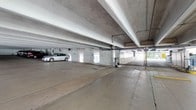 This single-level covered parking structure offers a functional and well-organized environment for vehicle storage and access. The facility features a smooth concrete floor throughout, providing a clean and durable surface suited for high-traffic use. Overhead, exposed structural beams and utility conduits run across the ceiling, reflecting a practical, no-frills architectural approach typical of purpose-built parking facilities.

The structure is equipped with a controlled-access gate at the entry point, enhancing security for users. ADA-compliant designated parking spaces are clearly marked, ensuring accessibility for all users. The open-air sides of the structure allow natural light to filter in, keeping the interior bright and well-ventilated without the need for extensive artificial lighting during daytime hours.

The layout is spacious, accommodating multiple vehicles with room for comfortable maneuvering. The perimeter walls are finished in painted concrete block, contributing to the structure's clean and utilitarian aesthetic. Overall, this parking structure provides a secure, accessible, and efficiently designed space that prioritizes ease of use, safety, and straightforward functionality for its occupants.