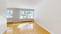 Located at 12 Park St E in Mississauga's charming Port Credit neighbourhood, this one-bedroom, one-bathroom unit offers a well-organized and efficient single-floor layout. Classic parquet flooring runs throughout the living spaces, lending warmth and a timeless character to the interior. The living room is a standout feature, showcasing a large picture window that floods the room with natural light and offers views of the surrounding streetscape, complemented by a baseboard heating unit beneath the sill. The separate dining area flows naturally from the living space, providing a defined area for meals. The galley-style kitchen is fitted with white cabinetry, a stainless steel sink, and full-size appliances including a refrigerator and stove, with in-unit laundry also present. The bedroom is a comfortable, well-lit room featuring its own window with a baseboard heater, parquet flooring, and access to closet storage. Multiple closets throughout the unit offer generous storage options. The bathroom is finished with full-height cream tile surrounding a soaker tub and shower combination, chrome fixtures, and a vanity with sink. The unit features two entrance points and maintains a clean, neutral palette throughout, creating a bright and functional living environment.