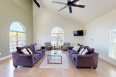 Located at 100 Dry Brook Rd in Wentzville, Missouri, this single-floor community space offers a well-appointed layout designed for both gathering and active living. The centerpiece is a grand great room distinguished by soaring vaulted ceilings, polished concrete floors, and dramatic arched windows that flood the interior with natural light. Exposed black ductwork adds an industrial accent against the soft sage-green walls, while large ceiling fans maintain airflow throughout the open expanse. The fully equipped kitchen features white cabinetry, granite countertops, stainless steel appliances, a subway tile backsplash, and a generous island with bar seating — ideal for social events and catered gatherings. The living area is furnished with plush seating arrangements anchored around a glass coffee table, with a wall-mounted flat-screen TV completing the lounge setting. A welcoming hallway entry provides a transition into the main space, accented with polished floors and comfortable seating. The dedicated gym is vibrant and functional, with bold teal-painted walls, arched windows, hardwood-style flooring, and a selection of cardio and strength equipment including treadmills, a stationary bike, and cable machines. Together, these spaces form a versatile and inviting community facility.