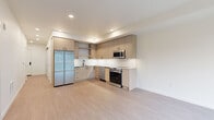 Located in Redmond, WA, this thoughtfully designed two-bedroom, two-bathroom residence offers a modern aesthetic with a cohesive palette of light tones and clean lines throughout. Light wood-style flooring flows seamlessly across the entire floor plan, unifying each room with a warm, contemporary feel.

The kitchen is a standout feature, showcasing flat-front cabinetry in a natural wood finish, a white subway tile backsplash, dark hardware accents, and a full suite of stainless steel appliances including a side-by-side refrigerator, electric range, microwave, and dishwasher. Ample upper and lower cabinetry provides generous storage.

The living area is bright and open, benefiting from a large picture window that invites natural light and frames views of the surrounding neighborhood. Both bedrooms are well-proportioned; the primary bedroom connects to a full en-suite bathroom featuring a double-sink vanity with wood cabinetry, a soaking tub, and floor-to-ceiling white tile surround. The second bedroom includes a sliding-door closet with built-in shelving. A second bathroom offers a single vanity with matching wood cabinetry and modern fixtures. Barn-style sliding doors add an additional contemporary design element to the hallways.