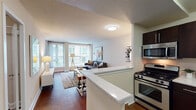 This single-floor residence is thoughtfully designed to maximize functionality and comfort across its key living spaces. The open-concept layout seamlessly connects the kitchen and living area, creating an inviting, cohesive environment ideal for both daily living and entertaining.

The kitchen is outfitted with dark espresso cabinetry, stainless steel appliances including a gas range, over-the-range microwave, and a full-size refrigerator, complemented by light stone countertops and a peninsula that serves as a natural divider between the kitchen and living space.

The living room is bright and airy, benefiting from large floor-to-ceiling windows that allow generous natural light to fill the room. Rich hardwood flooring runs throughout the main living areas, adding warmth and continuity to the space.

The primary bedroom features a bold teal accent wall, hardwood flooring, and a bright window with vertical blinds, creating a calm and stylish retreat. The secondary bedroom is equally well-lit with a large window and offers practical space for a desk and shelving. Both rooms maintain a clean, modern aesthetic.

The bathroom is finished with a dark wood vanity, a white countertop with an undermount sink, and a tub-shower combination. The overall design of the residence balances contemporary finishes with a warm, livable atmosphere throughout.