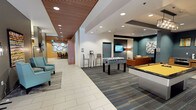 The lobby at 206 Bell St in Seattle, WA offers a welcoming and well-appointed common area designed for both relaxation and social interaction. The space features a contemporary aesthetic, highlighted by a distinctive slatted wood ceiling that adds warmth and texture, complemented by recessed lighting and clean white tile flooring that transitions into patterned carpet in the activity zones.

The game and recreation area serves as a central focal point, equipped with a full-size pool table and a foosball table, making it an ideal gathering spot for residents or guests. Adjacent to the game area is a comfortable lounge zone furnished with an orange sofa, wall-mounted television, and curated wall art, creating an inviting atmosphere for casual socializing.

A dedicated seating nook features bold textured orange wallcovering, a curved sectional sofa, and coordinating artwork, offering a more intimate setting for smaller gatherings or quiet relaxation. The main corridor area incorporates teal accent chairs and decorative wall installations, adding pops of color throughout. A reception counter area and elevator access are also visible, along with glass entry doors that allow natural light to fill the space. The overall design blends modern finishes with thoughtful amenity offerings, creating a functional and visually engaging lobby environment.