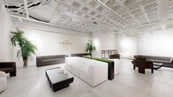 Located at 855 Main Street in Bridgeport, Connecticut, Soundview is a thoughtfully designed contemporary lounge space that blends industrial architecture with modern elegance. The single-floor layout offers an open, versatile environment ideal for gatherings, events, or collaborative use.

The space is defined by its striking exposed ceiling structure, painted entirely in white, which reveals an intricate grid of beams, ductwork, and track lighting. This industrial-chic overhead detail lends the room a sense of urban sophistication while allowing ample illumination throughout. Below, large-format marble-style porcelain tile flooring stretches across the entire space, contributing a clean, polished aesthetic that anchors the room's bright and airy atmosphere.

Seating is arranged in multiple distinct lounge vignettes, featuring a mix of plush white modular sofas, deep charcoal upholstered sectionals, and rounded boucle accent chairs. A central divider planter box filled with live greenery serves as a natural focal point and subtle room divider. Tall indoor palm trees and ornamental grasses add organic warmth and a resort-like ambiance to the otherwise minimalist palette.

A wall-mounted flat-screen display, a rustic wood-and-metal shelving unit, and sculptural coffee tables with glass and lacquered finishes round out the space. The gold Soundview logo displayed prominently on the main wall reinforces the brand identity of this well-appointed venue.
