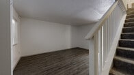This two-floor residence offers a well-organized layout with a variety of thoughtfully finished spaces across both levels. The kitchen is a standout area, featuring white shaker-style cabinetry, dark countertops, a tile backsplash, and a full suite of stainless steel appliances including a range, microwave, and dishwasher. Light wood-tone flooring runs throughout the kitchen, which also benefits from natural light and direct access to an outdoor area via a sliding glass door with vertical blinds. The living areas on the upper level showcase dark hardwood-style flooring and textured ceilings, with a staircase and open railing adding architectural interest. Bedrooms are carpeted for comfort and each include ceiling fans with lighting, natural light from windows, and closet access, lending a cozy and functional feel. The bathroom is finished with large-format taupe tile surrounding a soaking tub and shower combination, complemented by wood-look flooring and brushed nickel fixtures and towel bars. Clean white walls throughout the space create a bright, neutral backdrop that allows each room's distinct flooring and finishes to take center stage, resulting in a cohesive and move-in-ready environment.