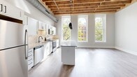 Located at 251 N Rose St in downtown Kalamazoo, MI, this one-bedroom, one-bathroom unit offers a distinctive loft-inspired aesthetic with thoughtful modern finishes throughout. The open-concept main living area seamlessly combines the kitchen, dining, and living spaces beneath striking exposed wood beam ceilings with visible ductwork, lending an industrial-chic character to the space. Large arched windows flood the area with natural light and provide views of the surrounding urban greenery.

The kitchen is well-appointed with white shaker cabinetry, granite countertops, a subway tile backsplash, stainless steel appliances, and a central island with pendant lighting above — ideal for both cooking and casual dining. Light wood-tone flooring flows throughout, complementing the warm tones of the overhead beams.

The bedroom offers a comfortable, private retreat with its own exposed beam ceiling detail and hardwood-style flooring. A sliding barn door opens to a dedicated closet with built-in shelving, adding both function and style. The bathroom features a full soaking tub and shower combo, framed by floor-to-ceiling subway tile, matte black fixtures, a granite-topped vanity, and wood-look flooring. In-unit laundry adds everyday convenience to this well-designed urban residence.