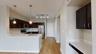 This single-floor residence is designed with an open, flowing layout that seamlessly connects the main living areas. The kitchen serves as a central hub, outfitted with rich dark espresso cabinetry that contrasts strikingly against light countertops and a full suite of stainless steel appliances, including a refrigerator, electric range, and built-in microwave. A white kitchen island with an integrated sink adds functional workspace and casual dining potential, while pendant lighting and a track lighting system overhead provide layered illumination throughout.

The living area extends naturally from the kitchen, featuring warm hardwood-style flooring, neutral gray walls, and a ceiling fan, creating a comfortable and versatile space. Track lighting continues into this area, ensuring consistent brightness throughout. A dedicated hallway leads to the private quarters, which include a carpeted bedroom equipped with a ceiling fan and a generously sized window that invites natural light and outdoor views.

The primary bathroom is well-appointed with dark cabinetry, a light countertop vanity, a soaking tub, and tile surround. A doorway from the bathroom opens directly into a spacious walk-in closet, adding practical storage. Hardwood-style flooring runs throughout the main areas, tying the space together with a cohesive, modern aesthetic.
