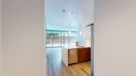 Unit 302 at 399 Fremont is a well-appointed 2-bedroom, 2-bathroom condominium spanning 780 square feet in San Francisco's Rincon Hill neighborhood. The open-concept kitchen and living area anchors the unit, featuring a Bosch stainless steel appliance suite—including a gas range, built-in microwave, and side-by-side refrigerator—paired with white gloss upper cabinetry, warm wood lower cabinets, and a white quartz island with pendant lighting. Light wood-tone flooring flows consistently throughout the unit. Floor-to-ceiling sliding glass doors in the living area and primary bedroom provide direct outdoor access to a private patio and a larger terrace, respectively, framing views of the surrounding San Francisco skyline and greenery. The primary bedroom measures 130 square feet and benefits from the same expansive glass wall. The second bedroom is well-sized with a large window. Both bathrooms are finished with white tile flooring, dark wood vanities with under-mount sinks, and wall-mounted medicine cabinets. A dedicated hallway connects the bedrooms and includes a closet for additional storage. The unit's clean, minimalist aesthetic is consistent throughout, creating a bright and functional urban living environment.