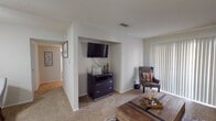 This single-floor residence offers a thoughtfully designed layout that balances comfort and functionality throughout. The living room serves as the heart of the home, featuring soft carpeted flooring, a built-in wall niche ideal for a television and media storage, and a large sliding glass door fitted with vertical blinds that allows ample natural light to fill the space. The kitchen is a standout area, showcasing slate-blue raised-panel cabinetry, light-toned countertops, a classic white subway tile backsplash, and wood-look vinyl flooring—combining both style and practicality. A dedicated dining area adjacent to the kitchen provides an intimate setting, complete with a ceiling fan overhead and easy access to the refrigerator. The bedroom is generously proportioned with plush carpet, a window for natural light, and a walk-in closet offering substantial storage. The full bathroom features a single-sink vanity with matching countertop finishes consistent with the kitchen, a shower-tub combination, and direct access to the in-unit laundry area, which is equipped with a full-sized washer and dryer. Textured ceilings are present throughout, adding a classic residential character to the overall ambiance of the home.