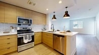 Located at 1040 N Grove St in Anaheim, CA, this well-designed one-bedroom, one-bathroom residence offers a thoughtfully laid-out single-floor plan with a clean, modern aesthetic throughout. Light wood-tone flooring runs through the main living areas, enhancing the bright and open atmosphere.

The kitchen is a standout feature, showcasing warm natural wood cabinetry, a geometric-patterned tile backsplash, and a full suite of stainless steel appliances including a gas range, over-the-range microwave, dishwasher, and a French door refrigerator. A peninsula with a white quartz countertop and dual pendant lights serves as both a prep area and casual dining space, seamlessly connecting the kitchen to the living room.

The bedroom is carpeted for comfort, features a window with slatted blinds for natural light control, and includes two closets for ample storage. The bathroom maintains the home's modern palette with a wood-framed vanity, white countertop, round mirror, a full soaking tub with shower, and a wood wall cabinet for additional storage.

A private balcony with bold yellow metal railings offers views of the surrounding contemporary multi-story building complex and landscaped courtyard below, providing an inviting outdoor retreat.