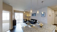 Located at 13195 West Progress Avenue in Littleton, Colorado, this single-floor residence offers a thoughtfully designed open-concept layout that seamlessly connects the living and dining areas. The space is finished with contemporary details throughout, including rich dark hardwood-style flooring that anchors the interior with warmth and elegance.

The living area is bright and inviting, centered around a comfortable seating arrangement and accented by a sliding glass door that opens to a private balcony equipped with a ceiling fan — ideal for enjoying Colorado's outdoor ambiance. Natural light filters generously through the large glass door, enhancing the airy feel of the space.

Overhead, a set of sleek pendant light fixtures with cylindrical glass shades illuminates the dining area, where a granite-topped counter or island serves as a natural focal point. The granite surface features a richly patterned design, adding a touch of sophistication to the space.

The interior walls are finished in neutral tones, providing a versatile backdrop that complements the modern décor. Thoughtful lighting placements throughout create a warm and welcoming ambiance, making this Littleton residence both functional and visually appealing for everyday living.