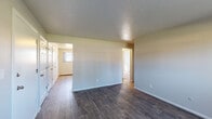 This single-floor unit offers a practical and functional layout, as revealed by the 3D floor plan overview. The main living area is open and spacious, finished with dark hardwood-style flooring that extends throughout most of the unit. Neutral-toned walls and a textured ceiling contribute to a clean, understated aesthetic. A wall-mounted air conditioning unit and baseboard heating provide year-round climate control.

The kitchen is well-appointed with white cabinetry, dark marble-patterned countertops, and a full suite of stainless steel appliances including a range, microwave, dishwasher, and refrigerator. A window above the sink brings in natural light, enhancing the workspace.

The bedrooms are carpeted for comfort and feature multiple windows that allow generous natural light and views of surrounding greenery. Baseboard heaters are present in each bedroom for individual climate control.

The bathroom is finished with clean white square tile surrounding a full bathtub and shower combination, complemented by chrome fixtures for a polished look. An entry area with closet space completes the unit's layout, offering convenient storage near the front door.
