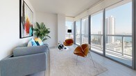 Suite 1606 is a thoughtfully designed high-rise residence that combines contemporary aesthetics with functional living. The open layout flows seamlessly across a single level, with clean white walls and light-toned tile and carpet flooring establishing a bright, cohesive atmosphere throughout.

The kitchen is a standout feature, equipped with stainless steel appliances including a French door refrigerator, electric range, built-in microwave, and dishwasher. Warm wood-grain cabinetry contrasted against white upper cabinets and light countertops lends a modern yet inviting character. A floor-to-ceiling window at the end of the kitchen frames expansive city and water views, flooding the space with natural light.

The living area continues this visual connection to the outdoors through large floor-to-ceiling windows offering panoramic skyline and bay views, creating an airy, elevated ambiance ideal for both relaxing and entertaining.

The bedrooms are carpeted and generously proportioned, with the primary bedroom benefiting from oversized windows that capture sweeping urban vistas. Both bathrooms feature wood-finish floating vanities, white countertops, large-format tile flooring, and tub-shower combinations with clean, minimalist detailing.