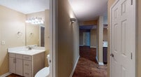 This single-story, 2-bedroom, 2-bathroom residence offers a thoughtfully designed layout with a cohesive blend of practical and aesthetic elements. Rich, dark hardwood flooring flows through the main living areas, contrasting warmly with the neutral tan walls and crisp white trim found throughout the home.

The living area benefits from vaulted ceilings and a ceiling fan, lending the space an open, airy feel. Natural light enters through windows dressed with blinds, enhancing the welcoming ambiance. A pass-through window connects the living area to the kitchen, which features dark espresso cabinetry extending to the ceiling, white countertops, a stainless steel sink, and stainless steel appliances including a range and over-the-range microwave.

A central hallway connects the bedrooms and bathrooms. The primary bedroom features vaulted ceilings, a ceiling fan, hardwood flooring, and direct access to its en-suite bathroom. The second bedroom offers plush carpeting, dual windows providing ample natural light, and a ceiling fan. Both bathrooms are finished with light wood vanities, white countertops, and hardwood-style flooring. The primary bath includes a soaking tub and walk-in closet access, while textured ceilings appear consistently throughout the home.