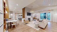 Located at 9000 Palm Passage Loop in Summerville, SC, this thoughtfully designed community clubhouse offers a generously proportioned, single-floor open-plan layout. The space is unified by light hardwood flooring, shiplap ceiling accents, and a cohesive coastal palette of whites, warm woods, and soft neutrals.

The central lounge area serves as the heart of the space, anchored by a modern electric fireplace with a crisp white surround, a wall-mounted flat-screen TV, and a large woven pendant light overhead. Comfortable seating arrangements and direct access to an outdoor area through full-length glass doors fill the room with natural light and views of the surrounding exterior.

The kitchen is a standout feature, showcasing an expansive marble-topped island with bar seating for multiple guests, white shaker cabinetry framed by warm wood accents, marble-style backsplash, and brushed gold fixtures — including a striking gold faucet and pendant lights.

A dedicated dining area provides multiple seating zones, including café-style round tables and a built-in banquette nestled beside floor-to-ceiling wood shelving and decorative botanical wallpaper. The welcoming entry foyer is framed by wall sconces and a natural wood credenza, creating a polished first impression for all who enter.