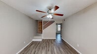 This two-story residence offers a well-organized layout with a blend of classic and practical design elements throughout. The kitchen is a standout feature, defined by a striking full-height exposed brick column that serves as a natural divider between the cooking and living areas. White cabinetry with decorative arched detailing lines one wall, complemented by light-toned countertops, a double sink, and black appliances including a range and refrigerator. Wood-look plank flooring runs consistently throughout the main living areas, adding warmth and continuity. The living room is open and airy, fitted with a ceiling fan and a staircase with white baluster railings leading to the second floor. A bedroom on the main level features a sliding glass door that opens to a private balcony with metal railings and views of the surrounding brick exterior. Upstairs, a spacious bedroom benefits from vaulted, sloped ceilings and dual bifold closets, offering generous storage. An additional bedroom on the upper level includes a large window and a ceiling fan. The bathroom is clean and functional, featuring a tub-shower combination with white tile surround, a built-in linen cabinet, vanity with a speckled countertop, and a wall-mounted mirror. The exterior balcony provides an outdoor retreat with a classic brick backdrop.