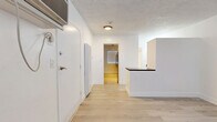 Located at 5119 Fountain Ave in the heart of Los Angeles, CA, this efficiently designed single-floor unit offers a thoughtful layout comprising a living room, kitchen, and bathroom. Light wood laminate flooring runs consistently throughout, lending warmth and visual continuity to the space.

The living area is bright and open, featuring white walls, a textured ceiling, a wall-mounted AC unit, and a large window with horizontal blinds that allows natural light to fill the room. The entry flows naturally into the rest of the unit, aided by a clean, minimal design aesthetic.

The kitchen is well-equipped with white cabinetry, dark granite-style countertops, a stainless steel gas range, a ventilation hood, and a striking dark subway tile backsplash. A window above the counter area brings in additional natural light and views of surrounding greenery. A peninsula counter separates the kitchen from the main living space, adding functional division without enclosing the area.

The bathroom is split into two areas: a vanity section with a floating white cabinet, dark countertop, dual mirrors, and a single sink; and a separate wet area with a soaking tub and shower combination, toilet, and a frosted window for privacy. The consistent light flooring ties both areas together seamlessly.

Overall, the space presents a modern, clean, and functional environment suited for comfortable urban living in Los Angeles.