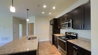 Located at 130 Ocean Aisle Circle in Salisbury, Maryland, this single-floor unit offers a clean, contemporary design with thoughtful finishes throughout. The kitchen is a standout feature, showcasing rich dark espresso cabinetry paired with light granite countertops that provide a striking visual contrast. A full suite of stainless steel appliances — including a refrigerator, electric range, and over-the-range microwave — lends a polished, modern aesthetic. The kitchen island is equipped with a stainless steel sink and pendant lighting overhead, adding both function and style. Recessed lighting throughout the kitchen ensures a bright, well-lit workspace. Light-toned hardwood-style flooring runs through the space, contributing to an open and airy feel. Neutral-toned walls complement the overall palette, creating a versatile backdrop that suits a variety of décor styles. The layout flows naturally, offering clear sightlines from the kitchen into adjacent areas of the unit. With its modern finishes and practical design, this single-level unit presents a comfortable and stylish living environment in Salisbury, MD.