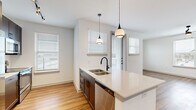 This thoughtfully designed one-bedroom, one-bathroom unit offers a cohesive open-concept layout that seamlessly connects the kitchen, dining, and living areas. Rich wood-look flooring runs throughout the entire space, lending warmth and visual continuity across every room.

The kitchen is a standout feature, showcasing dark espresso cabinetry, quartz countertops, a large center island with a double stainless steel sink and matte black faucet, pendant lighting, track lighting, and a full suite of stainless steel appliances including a French door refrigerator, microwave, and dishwasher. Multiple windows flood the kitchen and adjoining living area with natural light, while a ceiling fan adds comfort to the living space.

The bedroom is a calm, well-lit retreat with a large window and ceiling fan, finished in neutral tones. A dedicated walk-in closet provides generous storage with multiple shelving tiers and hanging rods. An in-unit stacked washer and dryer adds everyday convenience.

The bathroom is elegantly appointed with a dark wood vanity, white quartz countertop, matte black fixtures, a large mirror, and a soaking tub surrounded by marble-style tile. Clean white walls and modern hardware complete the refined aesthetic throughout this well-appointed unit.