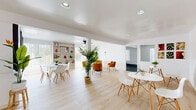 Located on Plummer Street in Northridge, Los Angeles, this single-floor community space offers a well-organized and thoughtfully designed layout across a comfortable footprint. The entrance welcomes visitors with light wood-style flooring, lush tropical plants, and an ornamental security door that sets a clean, modern tone.

The expansive living room serves as the heart of the space, combining a dining area featuring round white tables with Eames-style chairs, and a distinct lounge zone furnished with warm amber armchairs arranged around a circular coffee table. A ceiling fan overhead and recessed lighting throughout ensure the area remains bright and comfortable. Built-in shelving along one wall adds both function and character, while large windows with vertical blinds allow abundant natural light to fill the room. Colorful wall art and potted greenery contribute to the welcoming ambiance.

The exercise room is accessed directly from the living area and features durable concrete flooring, recessed lighting, and a wall-mounted air conditioning unit. It is equipped with a treadmill, elliptical trainer, and stationary bike, providing residents with convenient fitness amenities. The clean white walls and open layout make this a practical and well-appointed space for physical activity. Together, these rooms create a versatile, community-oriented environment with a fresh, contemporary aesthetic.