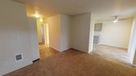 Located at 1015 112th St E, Unit E103 in Tacoma, Washington, this ground-floor unit presents a functional and comfortable single-level layout. The living area is generously sized, featuring warm neutral-toned carpet underfoot and a clean, open feel with soft natural light filtering through windows. The space flows naturally toward the kitchen and hallway, creating a connected and practical floor plan.

The kitchen stands out as a highlight of the unit, showcasing gray shaker-style cabinetry, light granite-patterned countertops, a stainless steel refrigerator, and a stainless steel electric range with overhead ventilation. Wood-look vinyl plank flooring runs throughout the kitchen, adding a modern contrast to the carpeted living areas.

The bedroom offers a comfortable, quiet retreat with plush carpet, a window with a baseboard heater beneath it for year-round comfort, and access to a well-sized walk-in closet equipped with a hanging rod and built-in shelving. The unit also includes what appears to be in-unit laundry hookups, adding a layer of everyday convenience. Neutral wall tones throughout keep the space feeling bright and move-in ready, offering a clean canvas for personalization.