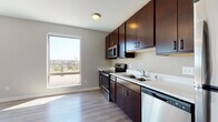 This single-floor unit offers a thoughtfully designed open-concept layout that seamlessly connects the living area and kitchen. The kitchen is well-appointed with rich dark espresso cabinetry extending to the ceiling, providing ample storage throughout. Light-toned countertops offer a striking contrast to the cabinetry, while a full suite of stainless steel appliances — including a refrigerator, electric range, built-in microwave, dishwasher, and double-basin sink — ensures full functionality. Durable hardwood-style flooring runs throughout the main living areas, contributing to a clean, cohesive aesthetic.

Large windows and a sliding glass door flood the living space with natural light and provide direct access to a private balcony, offering open outdoor views of the surrounding area. The living space is generously sized, allowing for flexible furniture arrangements.

The bedroom features plush carpeting, dual windows, a wall-mounted climate control unit, and a sliding-door closet. The bathroom is finished with a wide vanity featuring a white countertop, dark cabinetry below, a large mirror, and a full tub-shower combination with a curved curtain rod. Neutral wall tones and consistent finishes throughout contribute to a cohesive, modern ambiance.