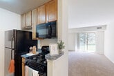 Located at 1101 Nalley Rd in Hyattsville, MD, this one-bedroom, one-bathroom residence offers a well-organized single-floor layout designed for comfortable everyday living. The combined living and dining area is bright and open, finished with plush wall-to-wall carpeting and anchored by a sliding glass door that floods the space with natural light and leads directly to a private balcony with outdoor views. The kitchen is efficiently designed in a galley style, featuring warm wood cabinetry extending to the ceiling, granite-style countertops, and black appliances including a gas range, built-in microwave, and refrigerator, all set on durable tile flooring. The bedroom is a comfortable retreat, carpeted and equipped with a ceiling fan, a window for natural light, and a double-door closet for ample storage. Two additional closets throughout the unit provide generous organizational space. The full bathroom includes a tiled tub-shower combination with a clean, neutral finish. The overall aesthetic is clean and neutral throughout, with white walls and light tones creating a bright, move-in-ready atmosphere. This residence combines practical storage solutions with a functional flow ideal for single occupants or couples.