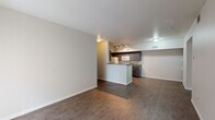 This single-floor unit offers a practical and well-organized layout designed for comfortable everyday living. The open-concept living area flows seamlessly toward the kitchen, connected by a peninsula counter that defines the two spaces while maintaining an airy, connected feel. Durable wood-look flooring runs throughout the main living and kitchen areas, providing a clean and cohesive aesthetic.

The galley-style kitchen is thoughtfully appointed with dark cabinetry, dark granite-style countertops, and white appliances including a refrigerator, electric range, microwave, and dishwasher. Track lighting illuminates the workspace, and ample upper and lower cabinet storage makes the kitchen highly functional. A window at the end of the kitchen corridor allows natural light to filter in.

The bedroom features neutral-toned walls, plush wall-to-wall carpeting, and a closet, offering a quiet and comfortable retreat. The bathroom is clean and straightforward, finished with wood-look flooring and a full tub and shower combination with white tile surround and chrome fixtures.

Throughout the unit, a neutral color palette of whites, grays, and warm tones creates a calm and versatile backdrop, making it easy to personalize the space to suit a variety of styles.