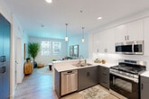 Located at 3100 Martin in Irvine, CA, Model A4 is a thoughtfully designed one-bedroom, one-bathroom residence that makes efficient use of its single-floor layout. The open-concept kitchen and living area serves as the heart of the home, featuring a modern kitchen outfitted with stainless steel appliances — including a gas range, built-in microwave, dishwasher, and refrigerator — complemented by two-tone cabinetry with white upper cabinets and charcoal lower cabinets, white quartz countertops, and light wood-style flooring. Pendant lighting adds a refined touch above the kitchen peninsula. The living area is bathed in natural light through large windows that frame views of the surrounding community, creating a bright and welcoming atmosphere. The bedroom offers a comfortable, carpeted retreat with a ceiling fan, dual closets, and direct access to the private balcony, which overlooks the community pool and palm-lined courtyard. The bathroom is finished with matching charcoal cabinetry, a wide vanity mirror, and a shower-tub combination. A dedicated in-unit laundry area adds everyday convenience. The space presents a clean, contemporary aesthetic throughout with a light, neutral color palette.