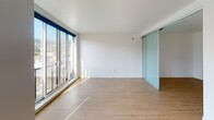 Located at 2121 NW Raleigh St in Portland, Oregon, this single-floor unit offers a thoughtfully designed layout with clean, modern finishes throughout. Light wood-tone flooring runs continuously through the space, complementing the crisp white walls and creating a bright, cohesive aesthetic.

The open living area is a highlight, featuring floor-to-ceiling sliding glass doors that lead to a balcony and invite abundant natural light while offering views of the surrounding Portland cityscape and hills. Frosted glass sliding panels provide flexible room division, adding a contemporary architectural touch.

The kitchen is well-appointed with dark wood grain cabinetry extending to the ceiling for ample storage, dark countertops, a subway tile backsplash in a soft seafoam hue, and a full suite of stainless steel appliances including a gas range, dishwasher, refrigerator, and over-the-range microwave.

A hallway connects the living areas to the bedroom, which features a sliding door closet with built-in shelving. The bathroom is finished with large-format taupe wall tiles surrounding a full soaking tub and shower combination, with chrome fixtures adding a polished detail. The unit's clean design and modern amenities make it a well-rounded space in the heart of Portland's Northwest neighborhood.