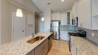 Located at 6010 Neal Trail Dr in Walkertown, NC, this single-story home offers a well-designed layout with modern finishes throughout. The kitchen serves as a central highlight, featuring vaulted ceilings that lend an open, airy feel. White shaker-style cabinetry with glass-front upper panels pairs with granite countertops, a subway tile backsplash, and a central island equipped with a sink and built-in shelving below. Stainless steel appliances, including a refrigerator, range, and microwave, complete the functional cooking space. Pendant lighting above the island adds a polished touch, while light hardwood-style flooring ties the kitchen together seamlessly.

The bedrooms are carpeted in a neutral tone and benefit from vaulted ceilings and ceiling fans, creating comfortable, well-ventilated spaces. Each bedroom includes windows with blinds that allow natural light and outdoor views. The bathroom includes a full tub-shower combination with clean white surround walls and tile flooring, maintaining a crisp, functional aesthetic throughout.

A dedicated laundry room with hardwood-style flooring, washer and dryer hookups, and a wire shelving rack provides practical utility space. Overall, the home presents a clean, neutral palette with thoughtful finishes suited for comfortable everyday living.